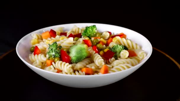 プレート上の野菜とスパイラルパスタは、黒の背景に回転します。緑のカリフラワーが皿に当たる — ストック動画