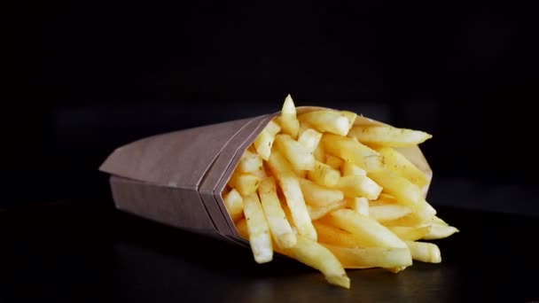French fries in a cardboard box on a black background revolves around itself. Fried potatoes — Stock Video