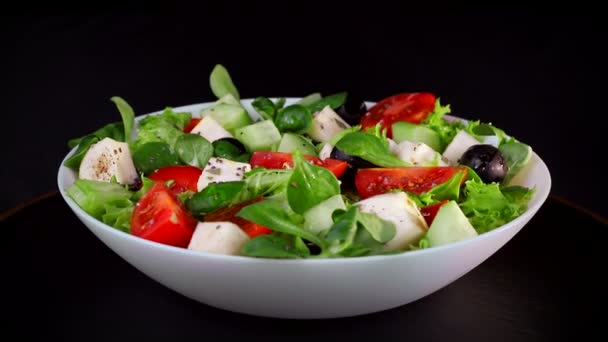 Dieta saudável. Salada de verdes e partes de tomates de queijo e pepinos. Placa gira sobre um fundo preto — Vídeo de Stock