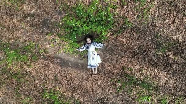 Letecký pohled na vrchol. Malá holčička leží na trávě s bílými květinami se zavřenýma očima. Kamera se pomalu vzdaluje a přibližuje se. Střela z dronu — Stock video