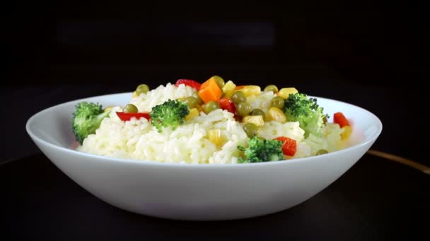 O arroz com partes de verduras, verdes e pimentão vermelho em uma chapa branca gira em um fundo preto — Vídeo de Stock