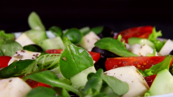 Dieta saludable. La ensalada de la verdura y los trozos del queso los tomates y los pepinos. El primer plano de la placa gira sobre un fondo negro — Vídeos de Stock