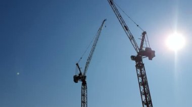 Mavi gökyüzü ve güneş arka planda iki inşaat vinçler, hangi inşaat vinç arkasında gizleme kamera parlar