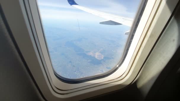 Door het raam van het vliegtuig te bekijken. De vleugel van het vliegtuig tegen de blauwe lucht en witte wolken. Achtergrond — Stockvideo
