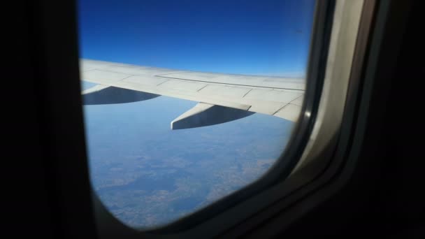 Вид через окно самолета. Крыло самолета против голубого неба и белых облаков. Фон — стоковое видео