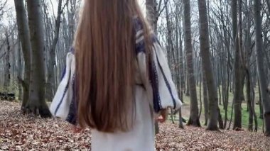 Mavi desenli açık elbiseli küçük bir kız kameraya sırtını dönerek ormana gider.