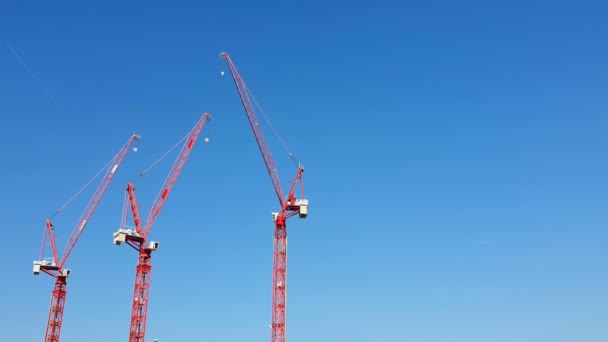 Tři stavební jeřáby červené barvy, které se přibližuje k modré bezmračné obloze. Pohled z výletní lodi — Stock video