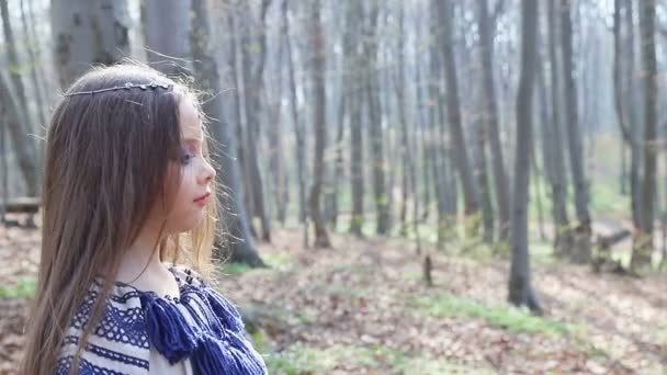 Liten flicka i en ljusblå klänning mönster sakta går i vår skogen. — Stockvideo