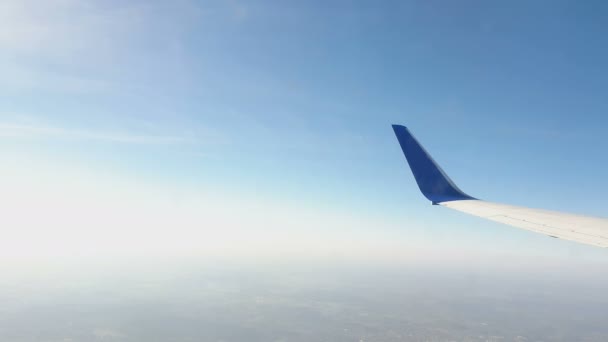 Vista a través de la ventana del avión. El ala de la aeronave contra el cielo azul y las nubes blancas. Contexto — Vídeos de Stock