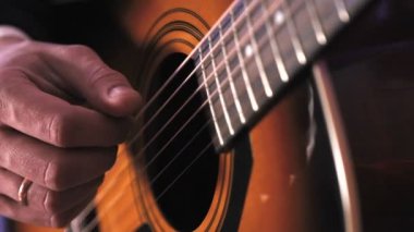 Bir adam akustik gitar çalar. Gitarın iplerine vuran elin yakın çekim