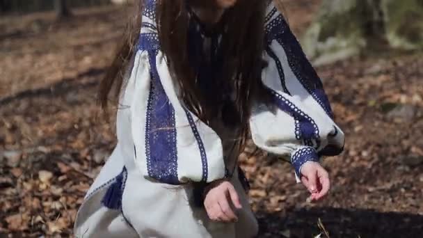 Una niña en el bosque coge un batidor de flores blancas del bosque y se lo pone en la cabeza. — Vídeo de stock