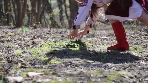 Маленькая девочка кладет венок из белых цветов на траву и уходит вдаль спиной к камере — стоковое видео