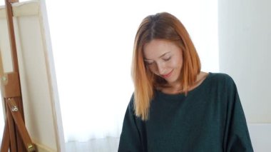 Utangaç bir şekilde gülümseyen ve aşağıya bakan bir kadın sanatçının portresi. Sanatçının düşünceli bir ifadesi var. Bir resim boyama süreci, çizmek için ilham arayan bir kadın