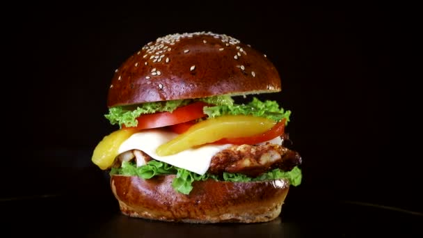 Burger egy nagy darab hús, zöldek és a sajt forog a fából készült hajón fekete háttér — Stock videók