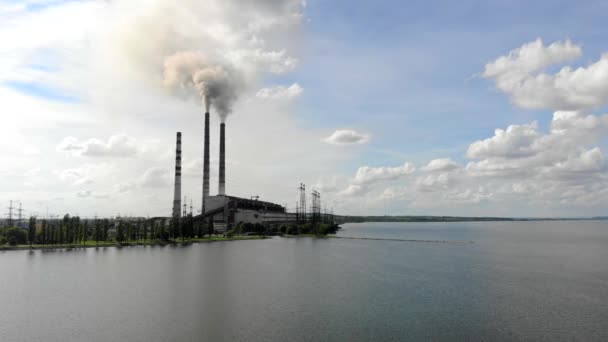 Luftbild Dichter dicker Rauch quillt aus Industrieröhren gegen den blauen Himmel und die Natur und einen großen See — Stockvideo
