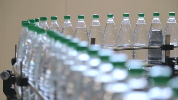 White plastic bottles stand on the water bottling line, filled with mineral water, and clogged with green caps — Stock Video