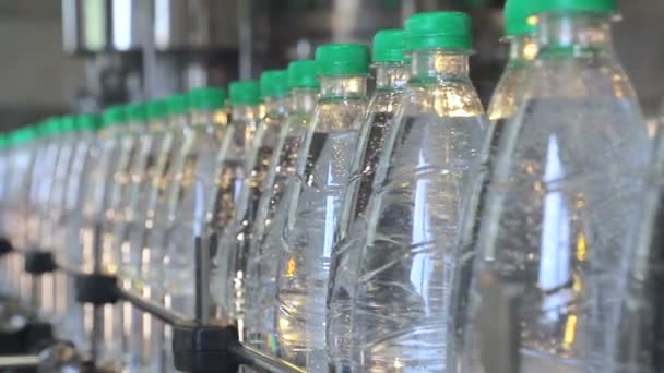 Botellas de plástico blanco de pie en la línea de embotellado de agua, lleno de agua mineral, y obstruido con tapas verdes — Vídeo de stock