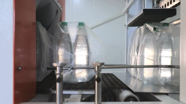 Embalagem automática de garrafas de plástico com filme na prensa de temperatura. Embalagem de garrafas para posterior transporte . — Vídeo de Stock