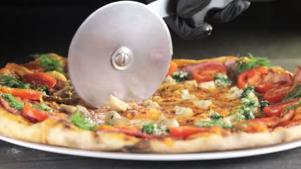 戴着黑手套的侍者将一个特殊的圆刀披萨切成碎片。刀在片子上的移动 — 图库视频影像