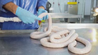 Mavi lastik eldivenli üretim işçisi, sosis yapıyor. Bir sosisin yakın çekimi bir çalışan tarafından oluşturulur