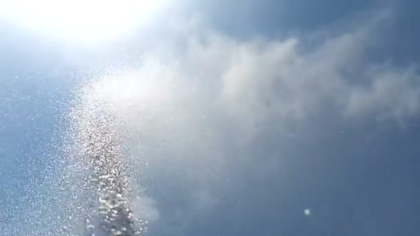 Mot bakgrund av den blå himlen med vita moln, en stråle av vatten i slow motion, strössel droppar runt. Bakgrund — Stockvideo