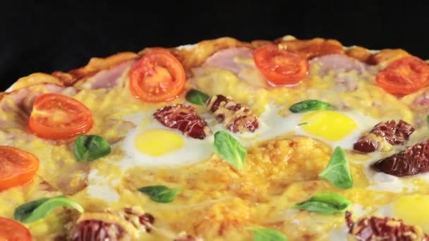 Крупным планом пиццы с сырными помидорами, колбасой и яйцом, вращающимся вокруг себя на черном фоне сверху — стоковое видео