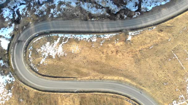 Vista aerea dalla cima della strada serpentina nelle montagne invernali, e le auto che si muovono sulla strada — Video Stock