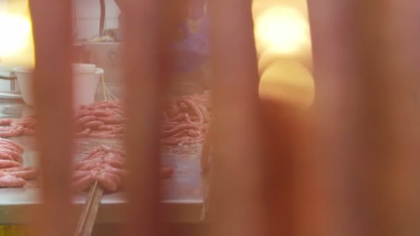 A look at the work because of the sausage hanging in the foreground. The foreground is blurred. Production of small hunting sausages of wild boars. Workers strung small sausages on the shelves — Stock Video
