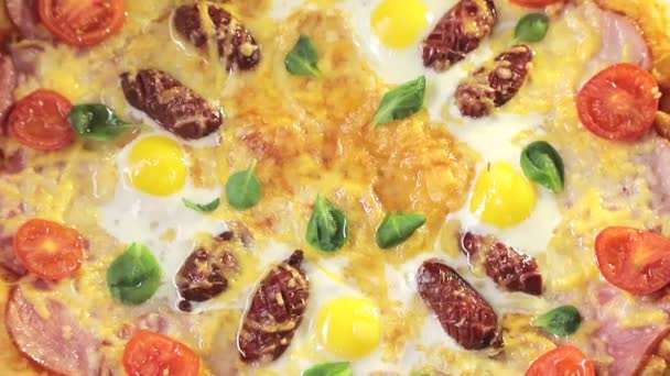 Pizza close-up con pomodori al formaggio, salsiccia e uova, che ruota intorno a sé, vista dall'alto — Video Stock