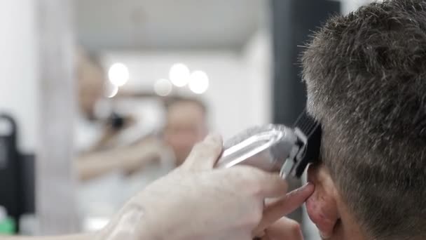 Fryzura męska w salonie fryzjerskim. zbliżenie w górę z a mistrz obcinanie a człowiek z czarny włosy z a obcinacz. — Wideo stockowe