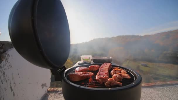 Кусочки мяса, курица, ребрышки, жареные на огне. Готовить мясо барбекю на крыше дома, против красивой панорамы . — стоковое видео