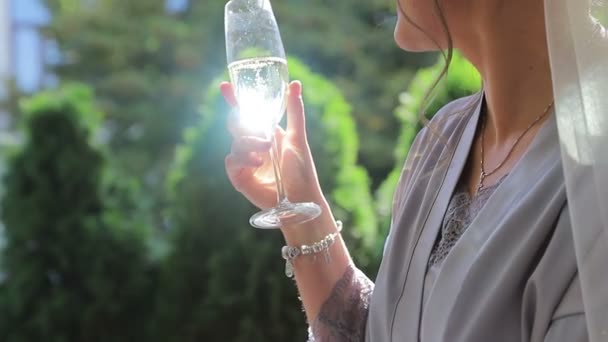 Een glas champagne in de hand van de meisjes. Een zonnestraal gloeit in een glas champagne. Het meisje drinkt uit een glas champagne. — Stockvideo