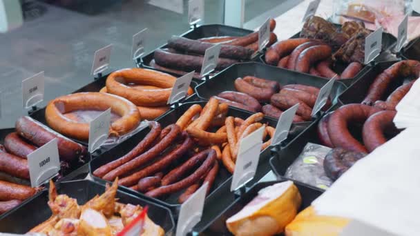 Many types of sausage lying in the window of a store or supermarket for sale. Sausage baked goods on the counter. — Stock Video