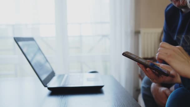 Un uomo e una donna fanno un ordine online attraverso un'applicazione in un telefono cellulare. Primo piano di tenere il telefono cellulare e lavorare con gadget a casa . — Video Stock