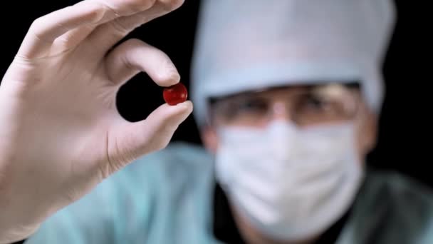 Médico cientista segura um comprimido vermelho em close-up contra um fundo preto . — Vídeo de Stock