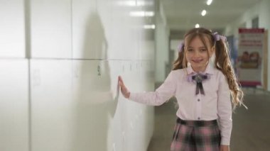Küçük bir öğrenci okul koridorunda dolapların yanında yürüyor..