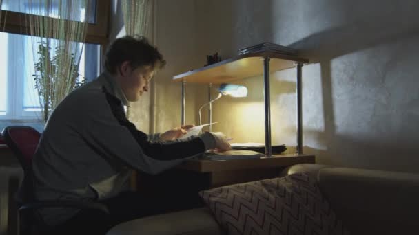 Étudiant homme d'affaires travaillant dans une pièce sombre avec une lampe de bureau avec des documents. L'élève résoud ses devoirs dans sa chambre le soir . — Video