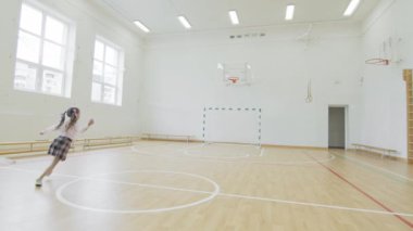 Okulun spor salonunda koşan küçük kız. Spor yapmayan bir kız. Spor salonundaki mutlu kız öğrenci.