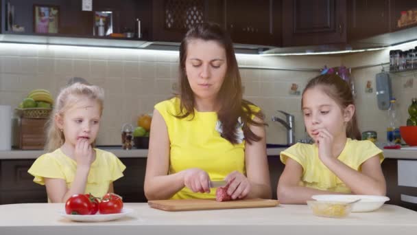 Anne ve çocuklar mutfakta yemek pişiriyor. Küçük kız pizza hamurunu pürüzsüz yapıyor. Annem çocuklara pizza pişirmede yardım eder.. — Stok video