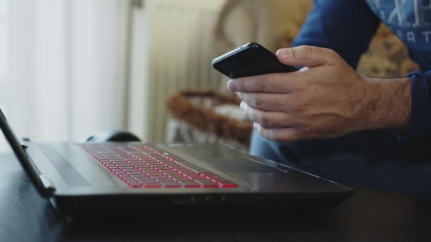 Businessman tiene in mano un telefono cellulare e preme sul touch screen. Uomo che lavora a casa con cellulare e laptop . — Video Stock