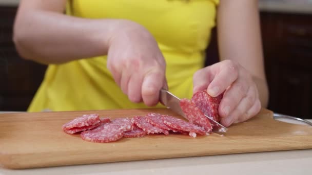 Женщина готовит куски колбасы с ножом на деревянной доске — стоковое видео