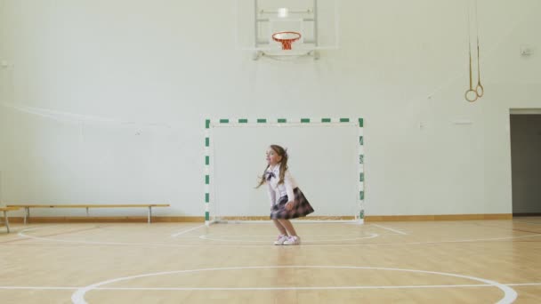 Mała dziewczynka siedzi na sznurku w szkolnej siłowni. Dziewczyna wykonuje sznurek gimnastyczny w siłowni. — Wideo stockowe