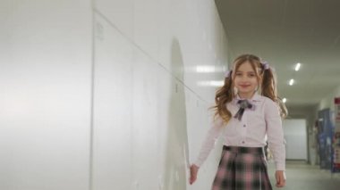 Küçük bir öğrenci okul koridorunda dolapların yanında yürüyor..