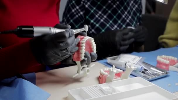 Zahnarzt in schwarzen Handschuhen Nahaufnahme auf einer Attrappe eines Skeletts von Zähnen mit einer Bohrmaschine. der Zahnarzt übt geschickt die Ausrichtung der vorderen Zähne auf das Layout — Stockvideo