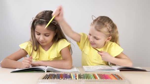 Grappige en grappige kinderen. Kinderen aan tafel dansen en creëren. Twee kinderen zitten aan een tafel en kleuren een kleurboek. — Stockvideo