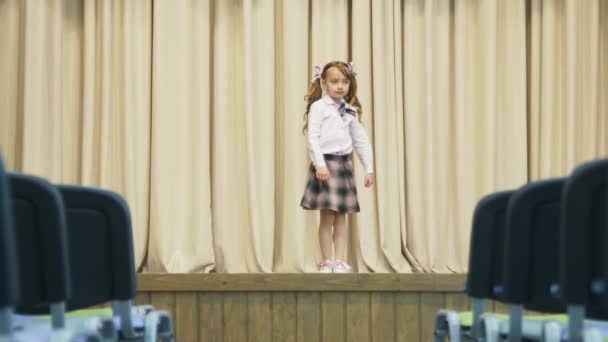 Mała dziewczynka na scenie w holu bez ludzi. Dziewczyna obraca się wokół siebie.. — Wideo stockowe