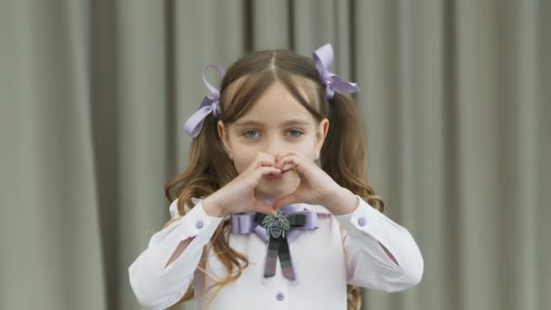 La petite fille montre un cœur avec ses mains et regarde émotionnellement la caméra . — Video