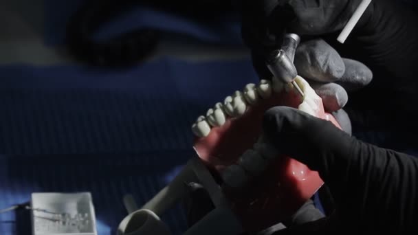 Dentista con guantes negros Primer plano de una maqueta de un esqueleto de dientes usando una máquina perforadora. el dentista practica hábilmente alinear los dientes delanteros en el diseño — Vídeos de Stock