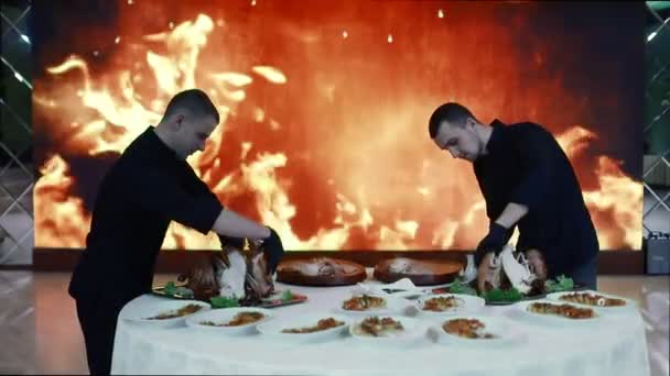 Šéfkuchaři krájejí čerstvě uvařené maso na pozadí velké obrazovky s umělým ohněm. Diskotéka. Světlo různých barev osvětluje scénu. — Stock video