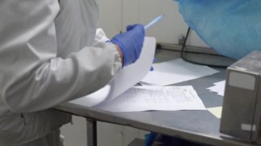 Şirketin bir çalışanı, malları şirketten almış ve belgeleri mavi eldivenle inceliyor..
